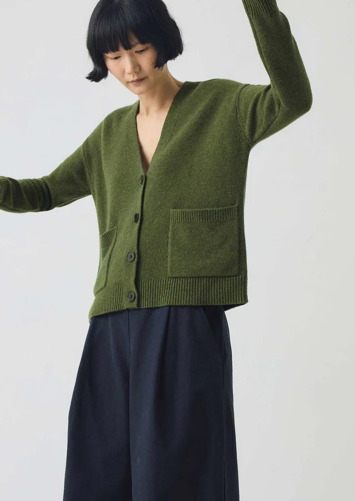 Person wearing a green cardigan and dark pants on a white background