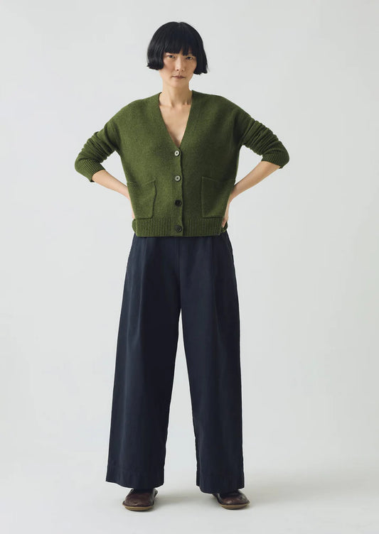 Person wearing a green cardigan and dark pants on a white background