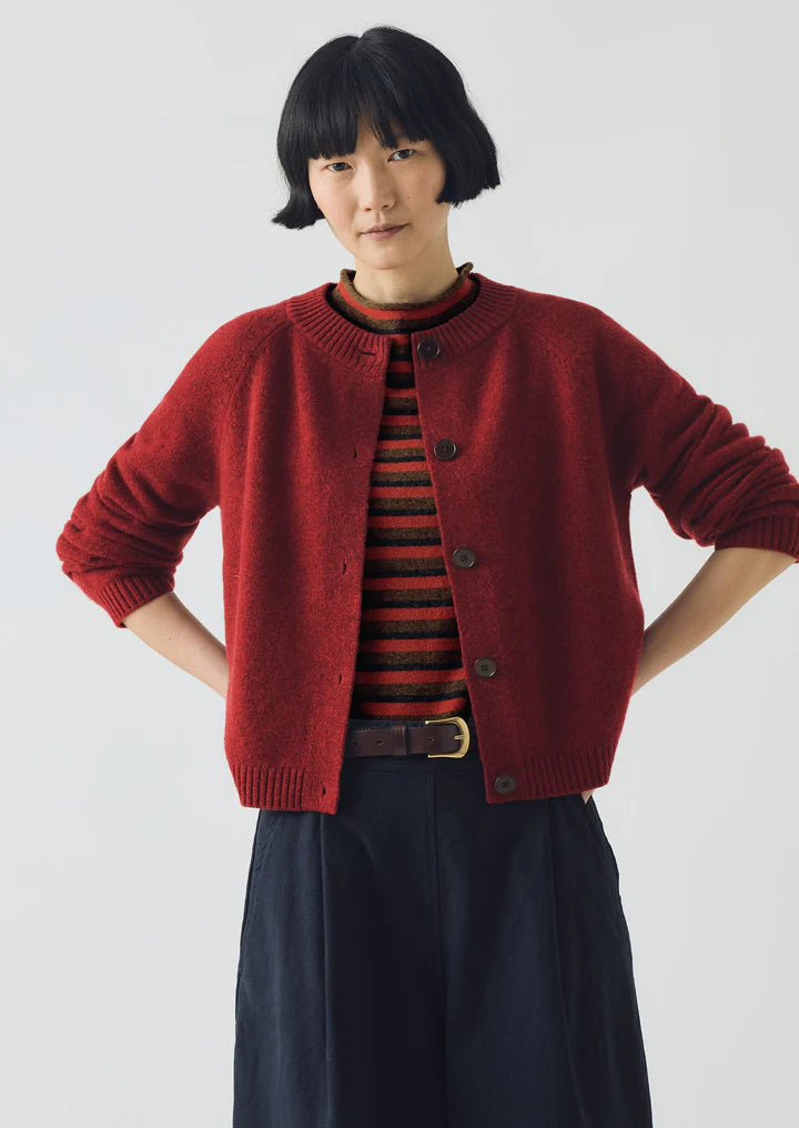 Person wearing a red cardigan over a striped shirt with a plain background