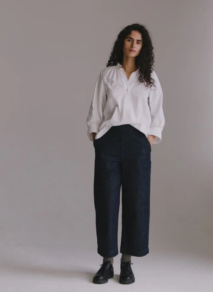 Person wearing a white shirt and dark pants against a plain background