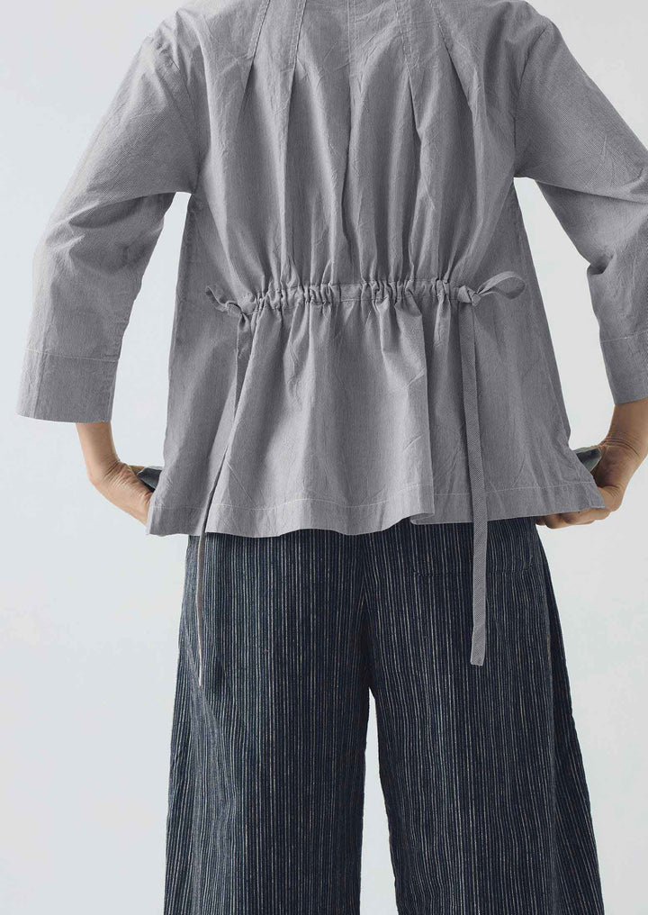 Person wearing a gray top with a drawstring waist and dark striped pants on a light background