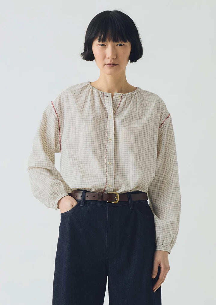 Person wearing a beige checkered blouse and dark pants on a white background