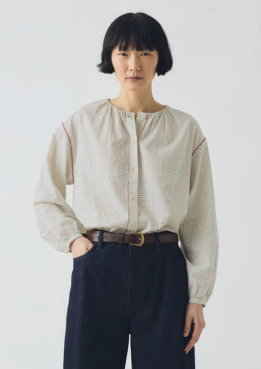 Person wearing a beige checkered blouse and dark pants on a white background