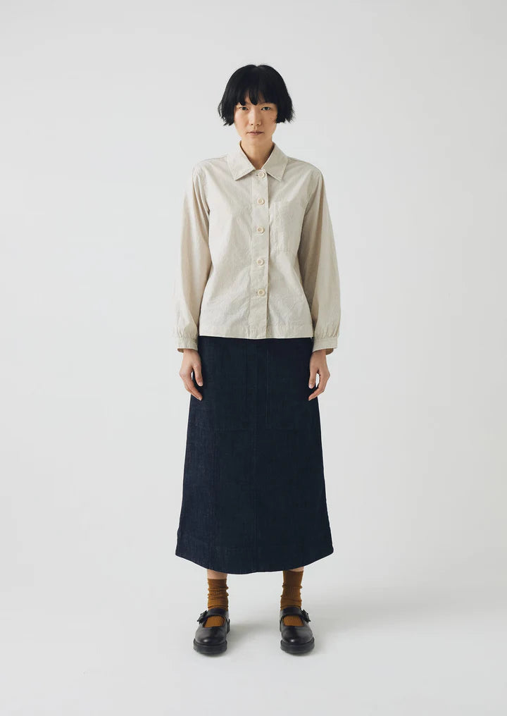 Person wearing a beige shirt and navy skirt on a white background