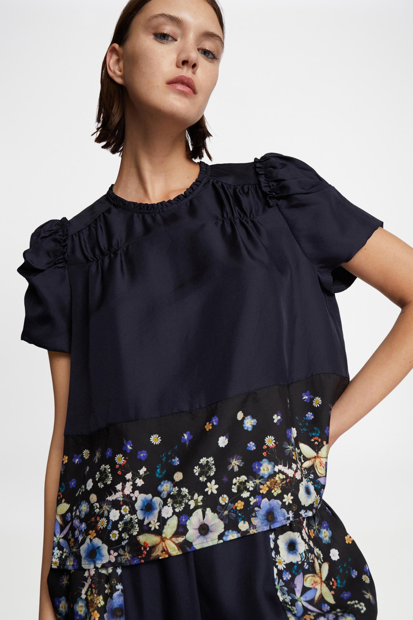 Model wearing navy blue short sleeve silk blouse with floral border at the waist.