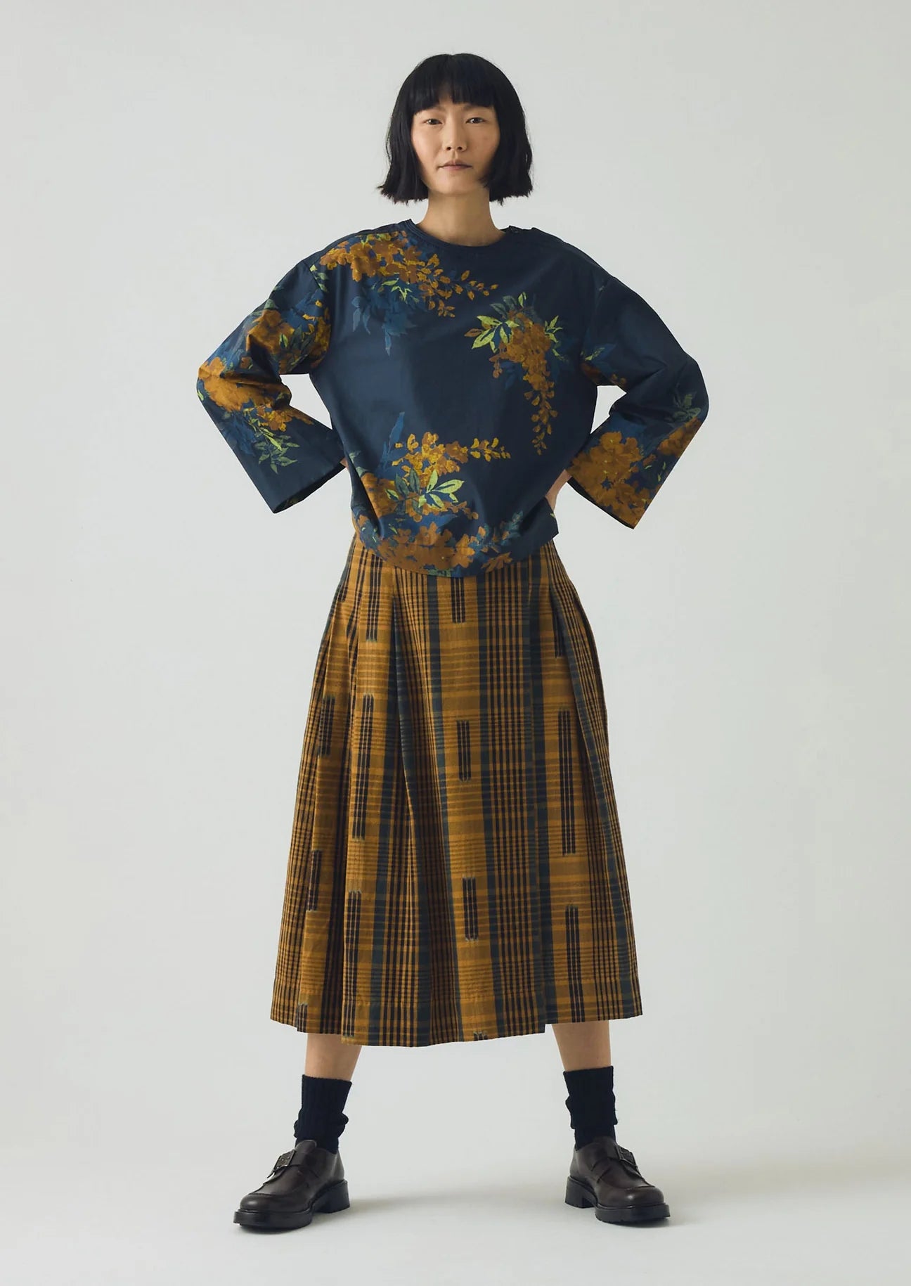 Person wearing a dark blue floral top and patterned skirt on a white background