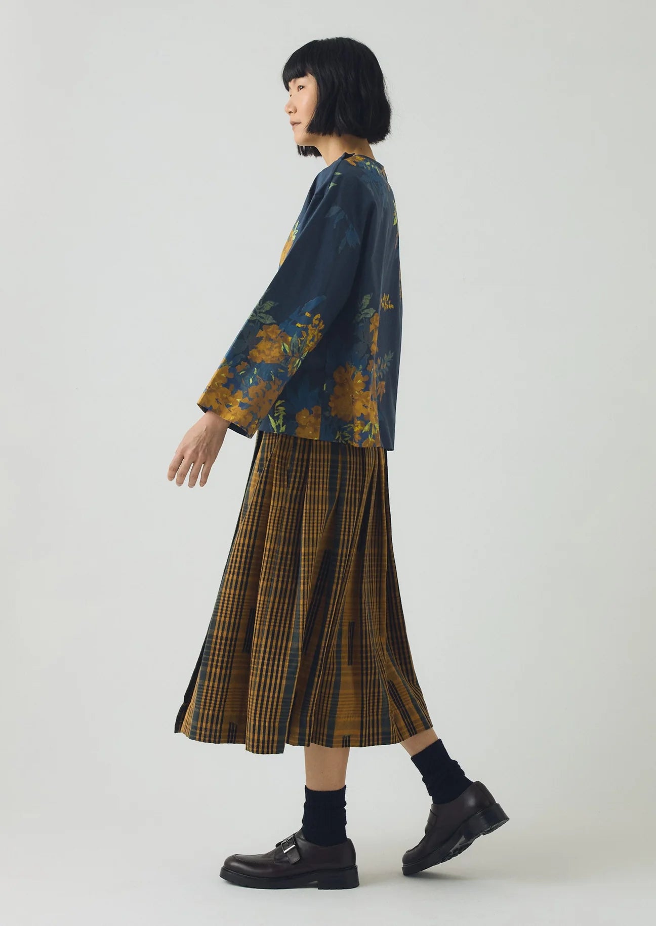 Person wearing a floral blouse and plaid skirt on a white background