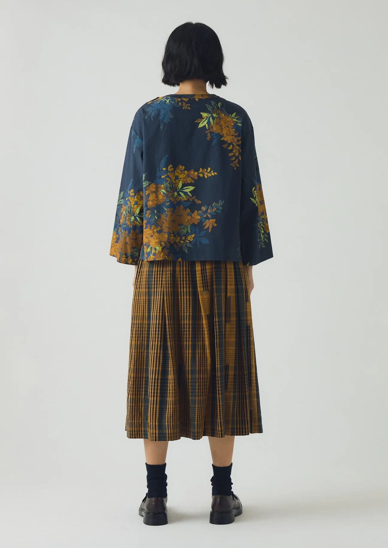 Person wearing a floral top and plaid skirt on a white background