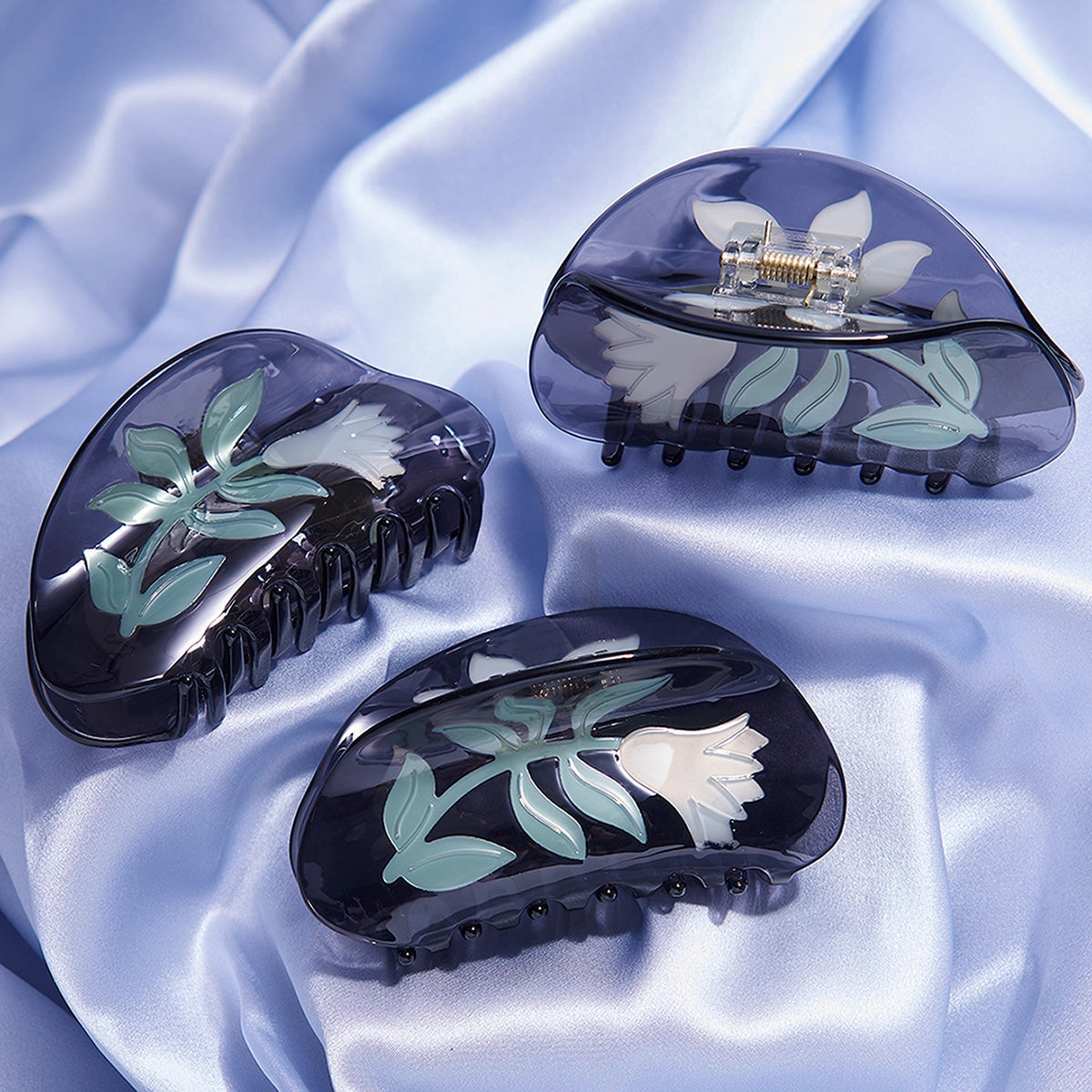 Three black hair clips with floral designs on a light blue fabric background