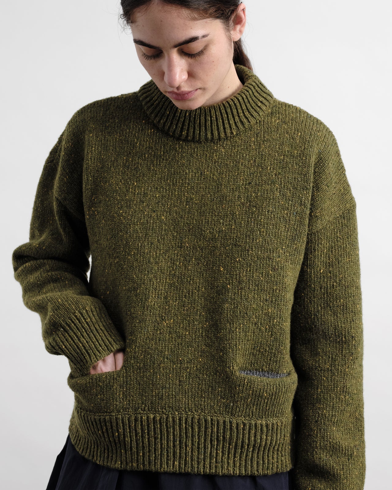 Person wearing a green knitted sweater against a white background