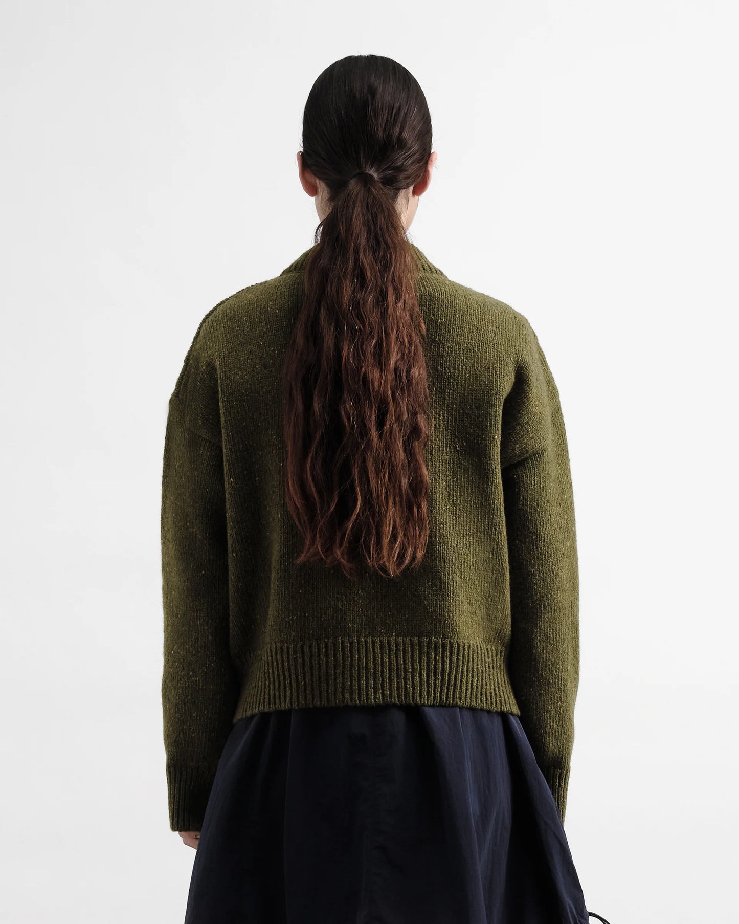 Person wearing a green sweater with long hair in a ponytail on a white background