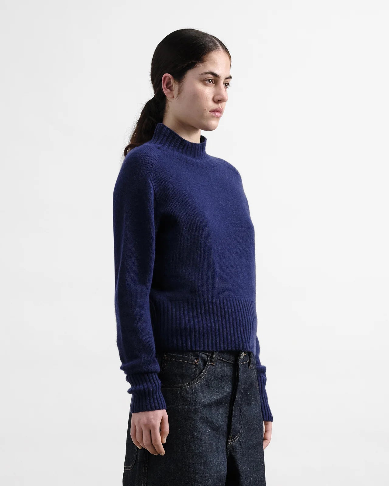Person wearing a blue sweater and dark jeans on a white background