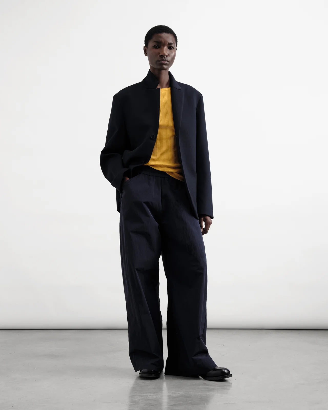 Person wearing a navy Jacket and pants with a yellow shirt against a white background