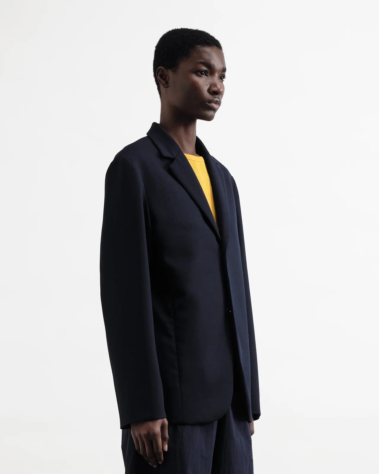 Person wearing a dark coat over a yellow shirt on a white background