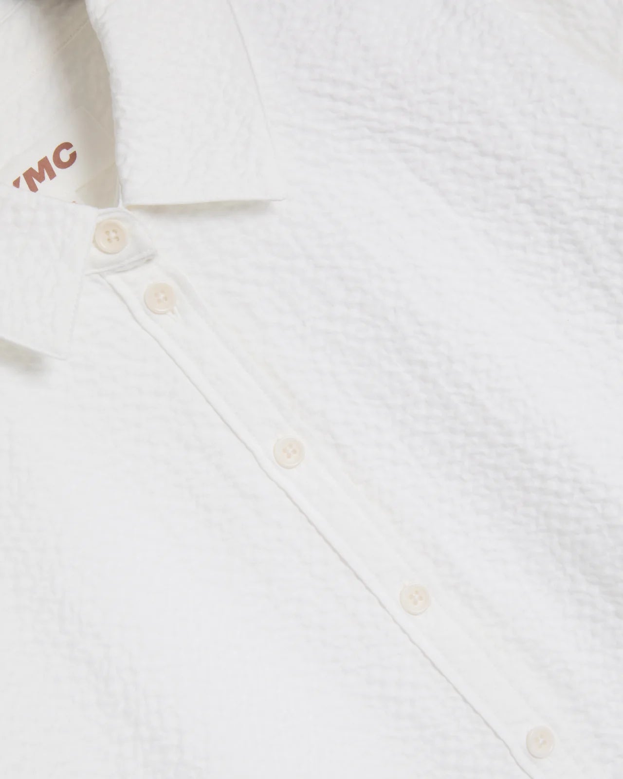 Close-up of a white textured shirt with buttons and a brand logo on a white background
