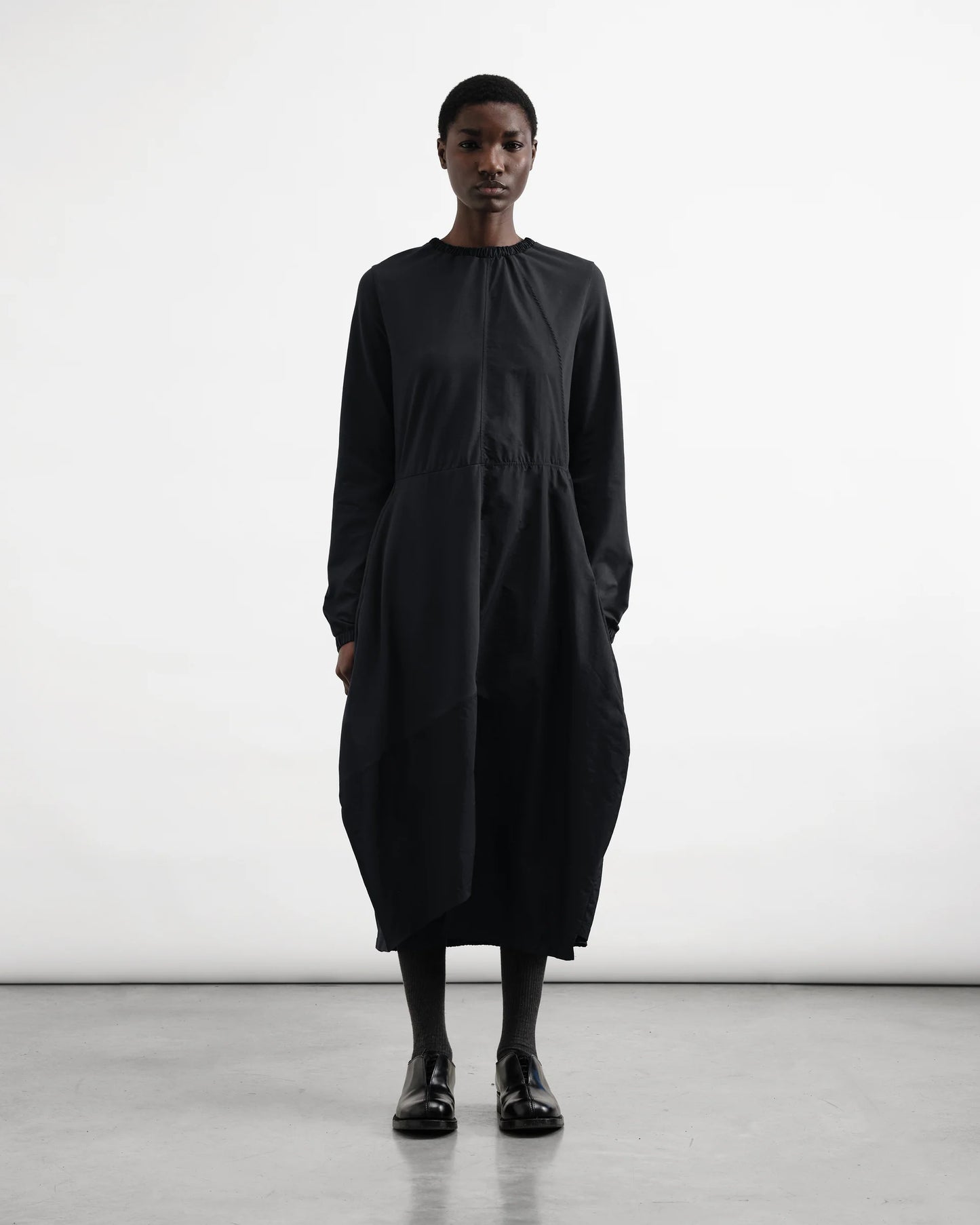 Person wearing a black dress standing against a white background