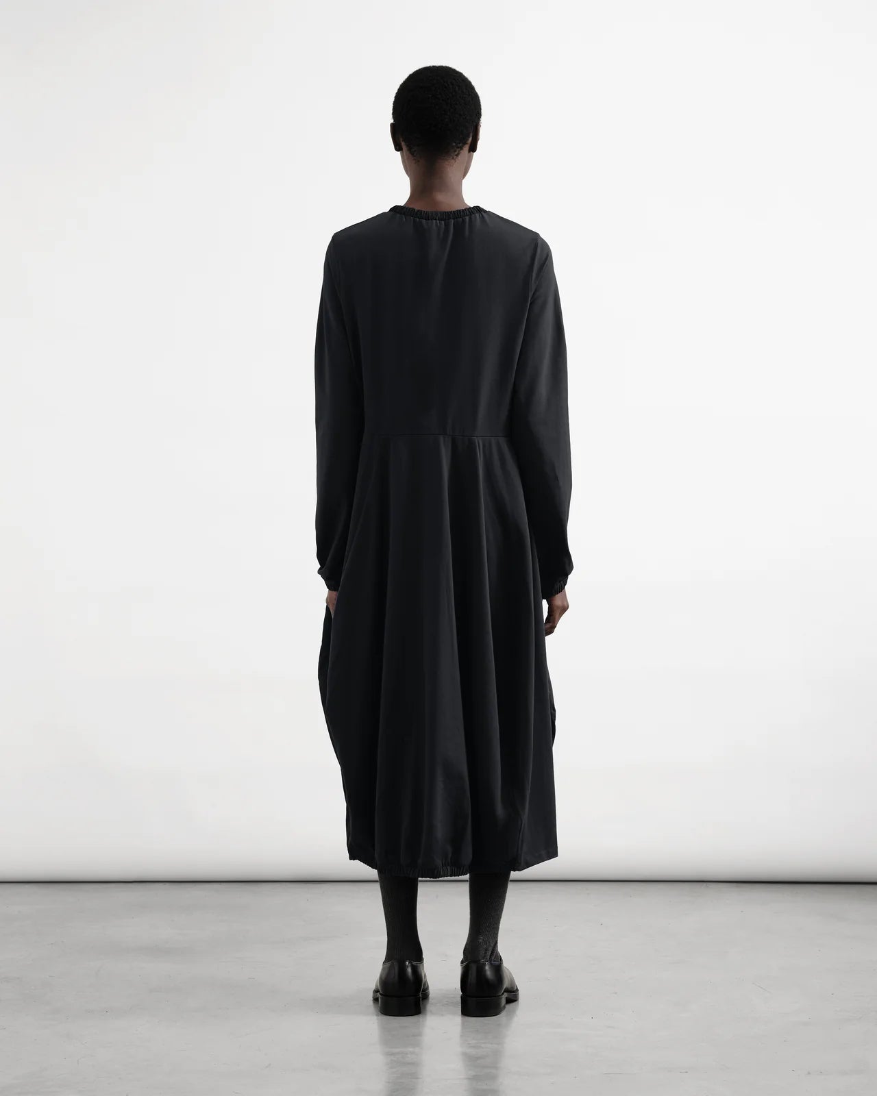 Person wearing a black dress standing against a white background