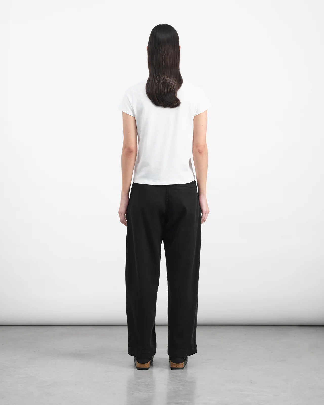 Person wearing a white shirt and black pants against a plain background