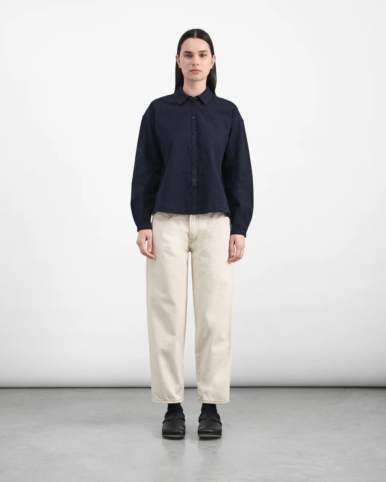 Person wearing a navy shirt and beige pants on a white background