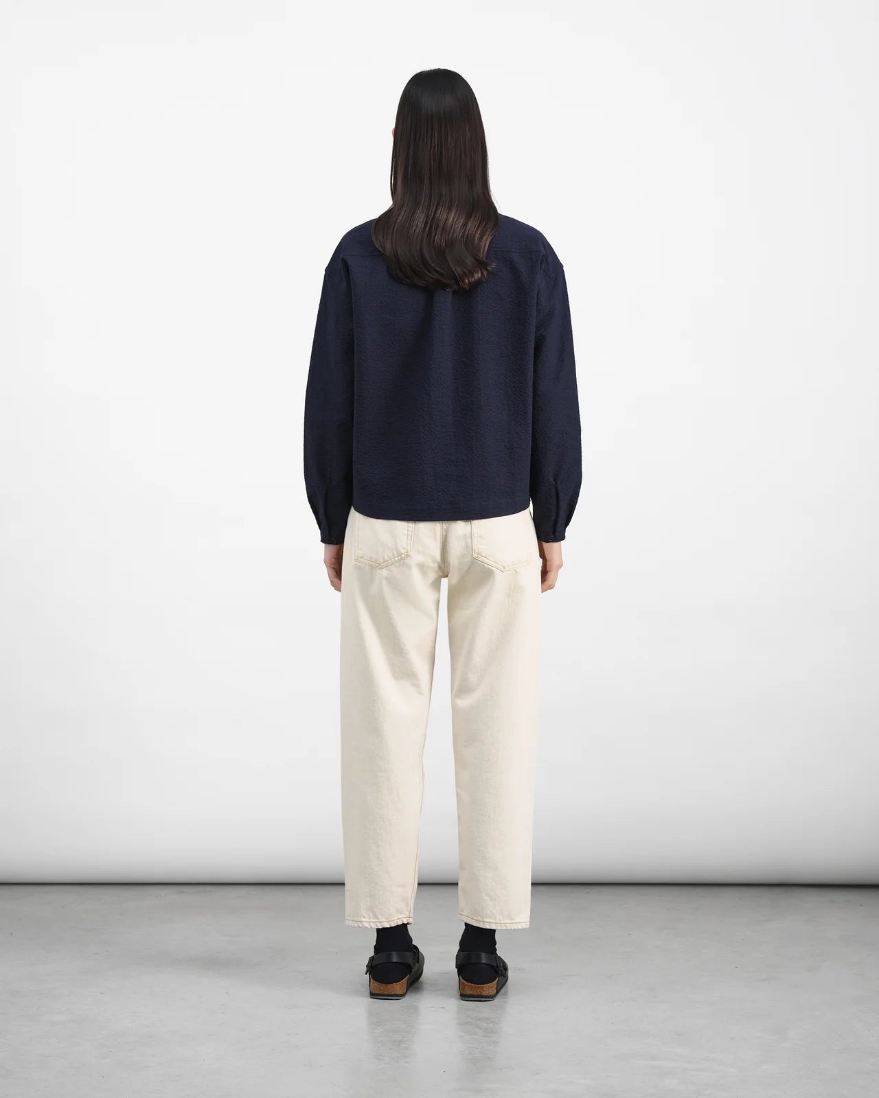 Person wearing a navy sweater and white pants standing against a plain white background