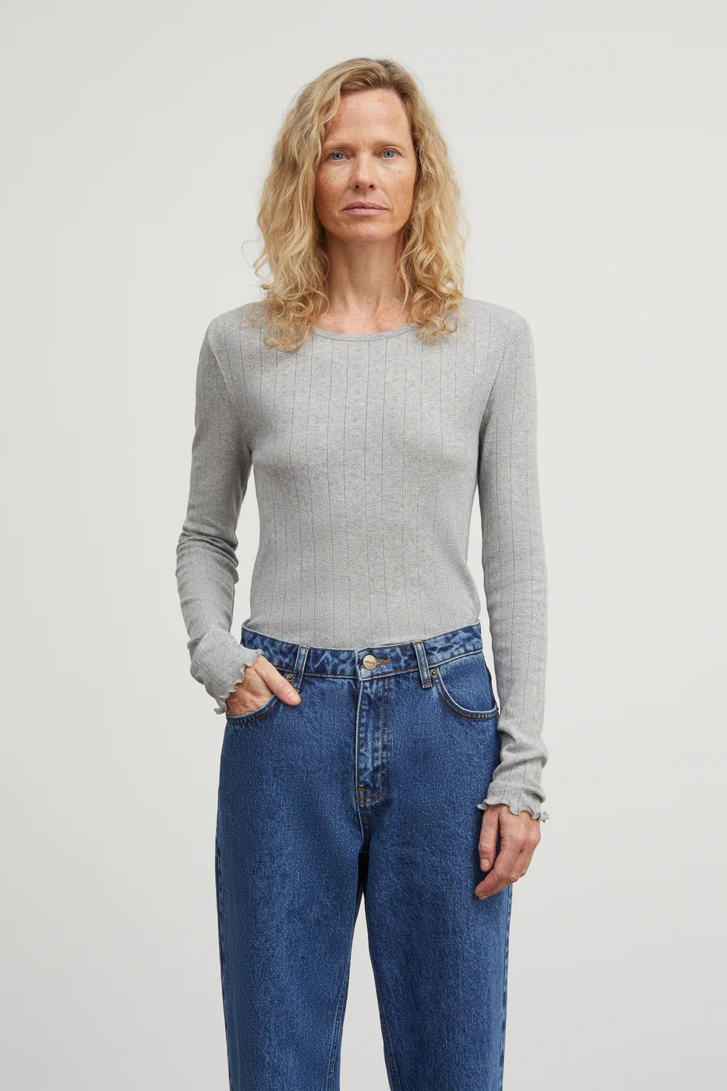 Woman wearing a gray sweater and blue jeans against a plain background