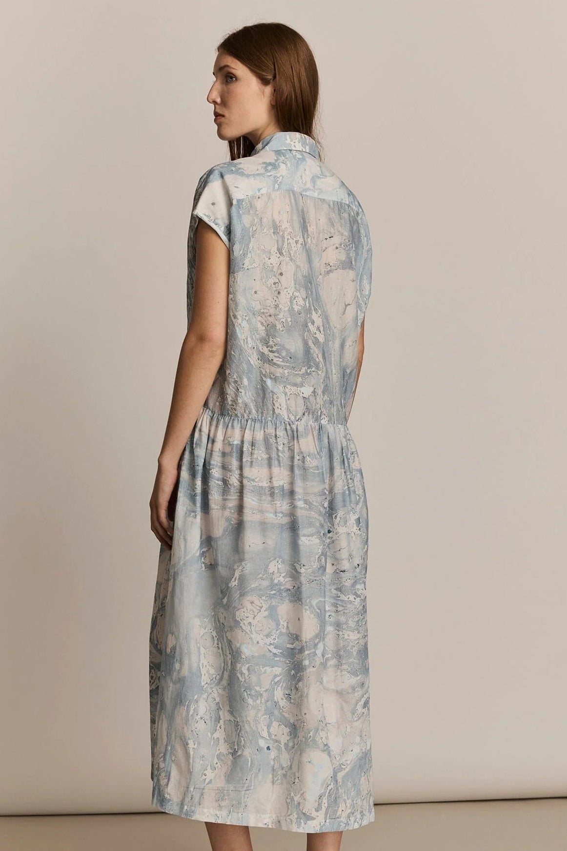 Woman wearing a light blue patterned dress on a beige background. Back view
