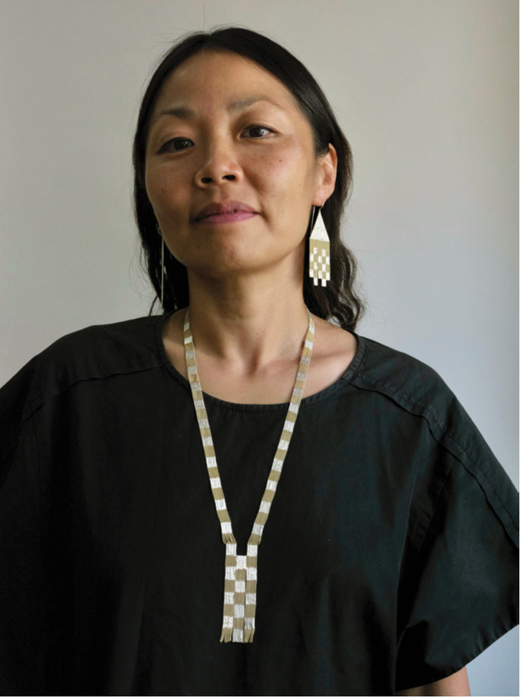 A woman shown wearing sterling silver and brass patterned earrings and a matching necklace,