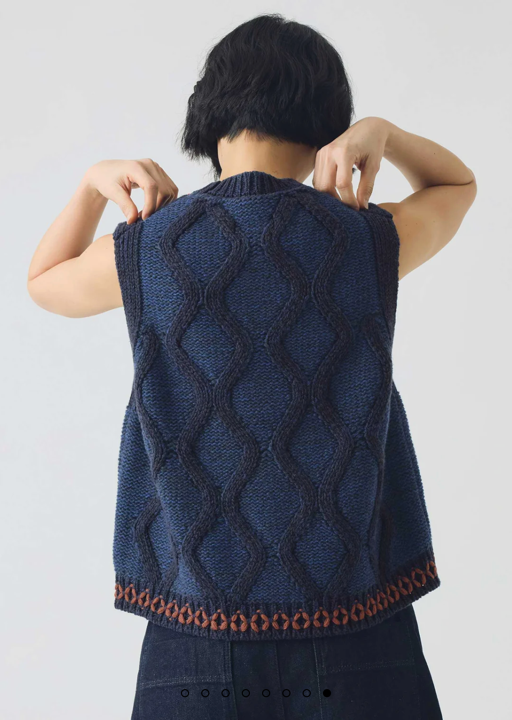 Rear view of person wearing a blue knitted vest with a geometric pattern on a white background