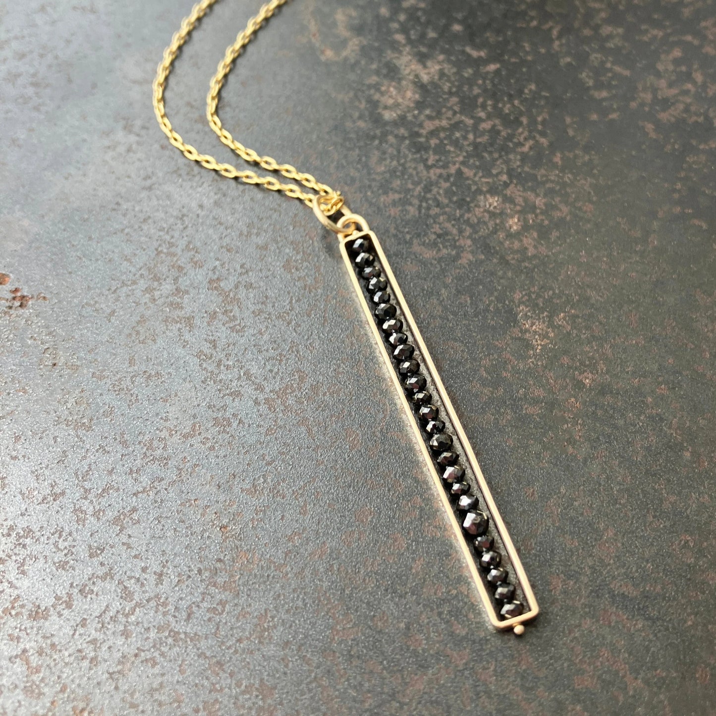 Gold necklace with black beads on a textured surface