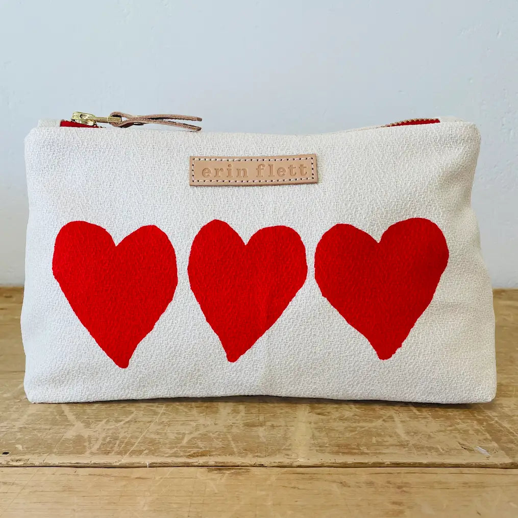 White pouch with three red hearts on a wooden surface and light gray background