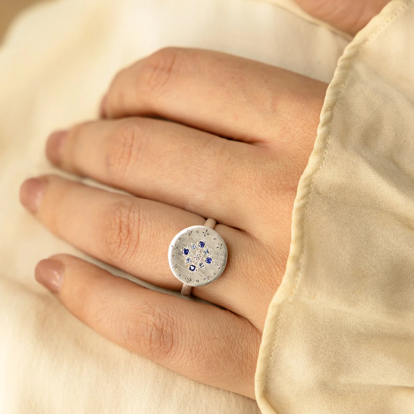 Silver ring with gemstones on a hand against a beige background