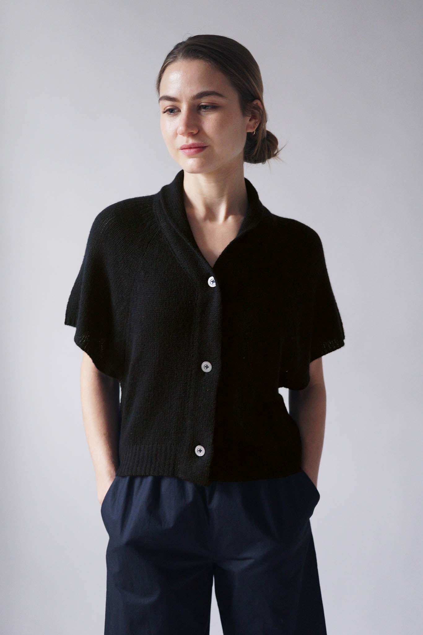 Black cashmere short sleeve three button cardigan. V-Neck with shawl collar and cropped to waist length. worn with navy pleated pants