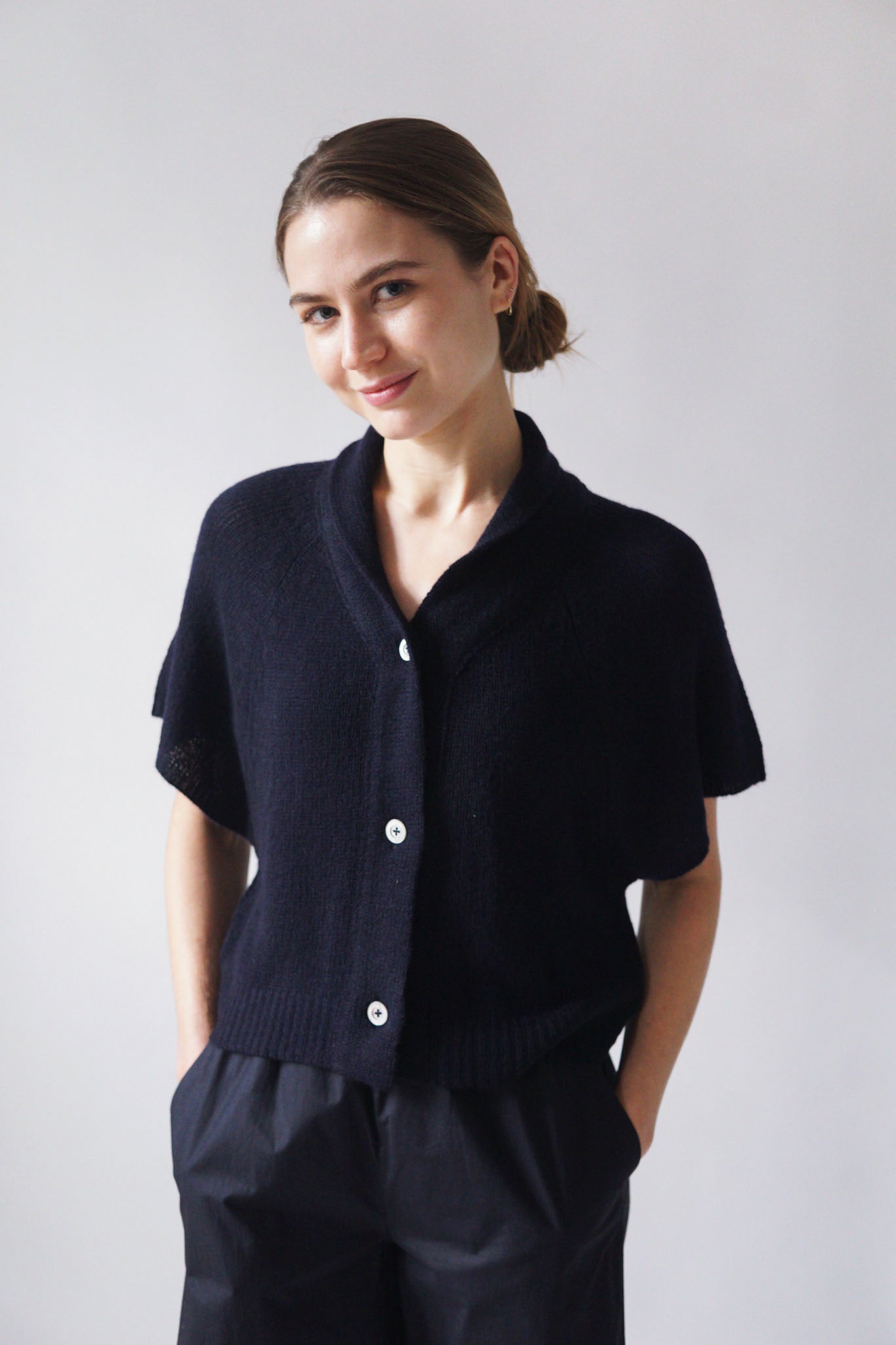Navy cashmere short sleeve three button cardigan. V-Neck with shawl collar and cropped to waist length. worn with navy pleated pants