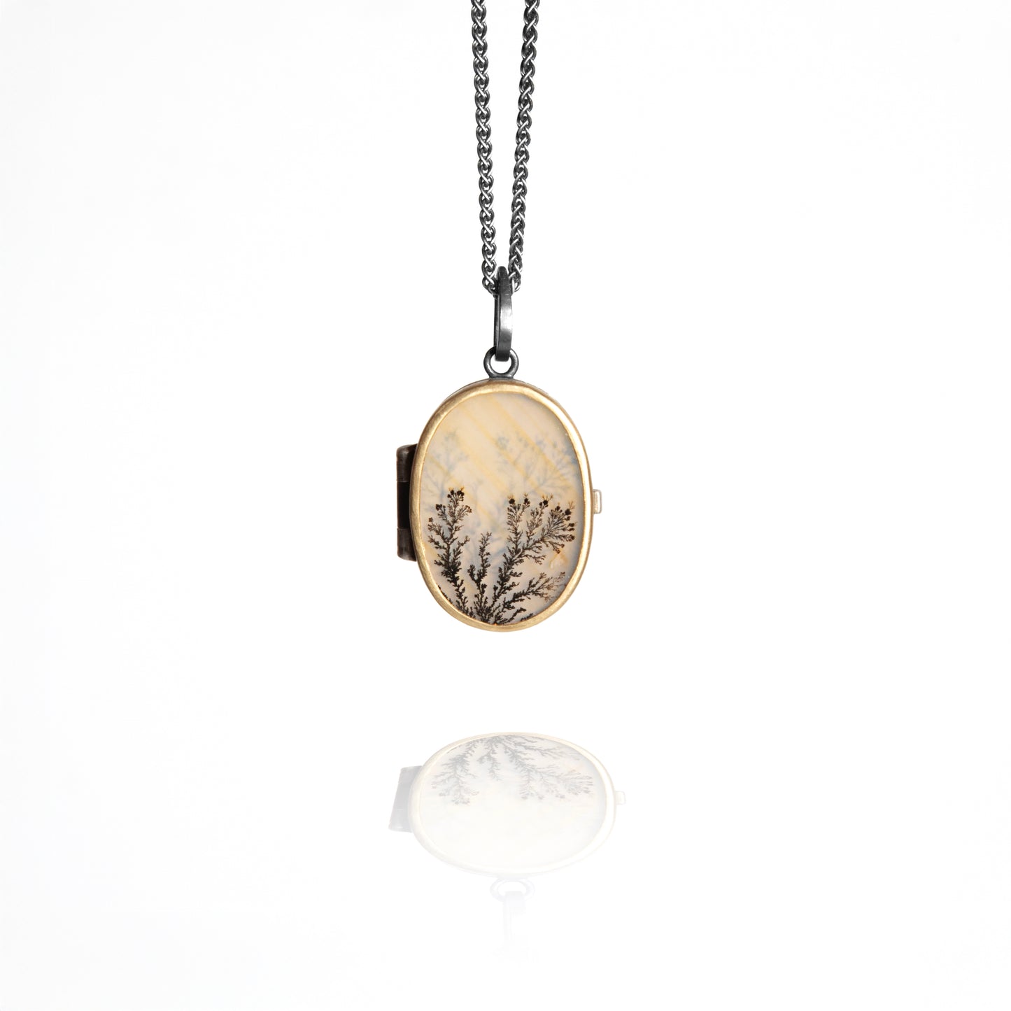 Oval locket with nature-themed design on a chain against a white background