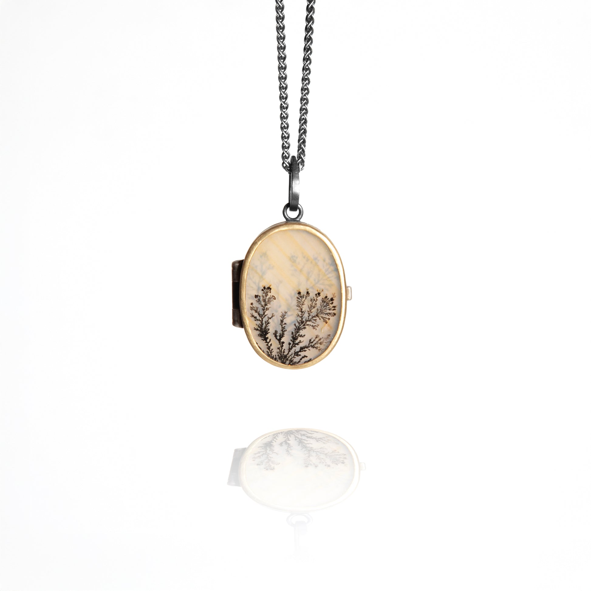 Oval locket with nature-themed design on a chain against a white background