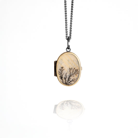 Oval locket with nature-themed design on a chain against a white background