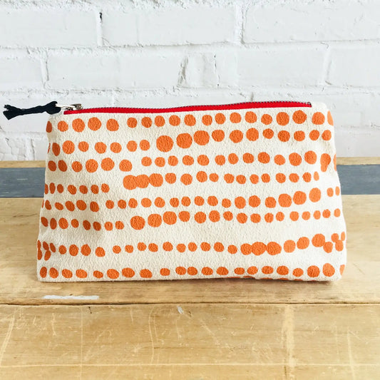 Pouch with orange polka dot pattern on a wooden surface and white brick wall background