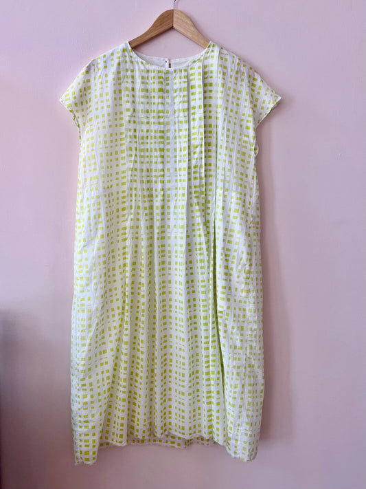 White dress with green pattern on a wooden hanger against a pink background