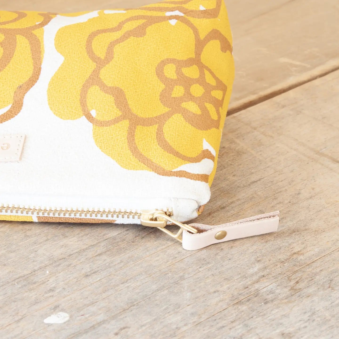 Yellow floral pouch with a gold zipper on a wooden surface