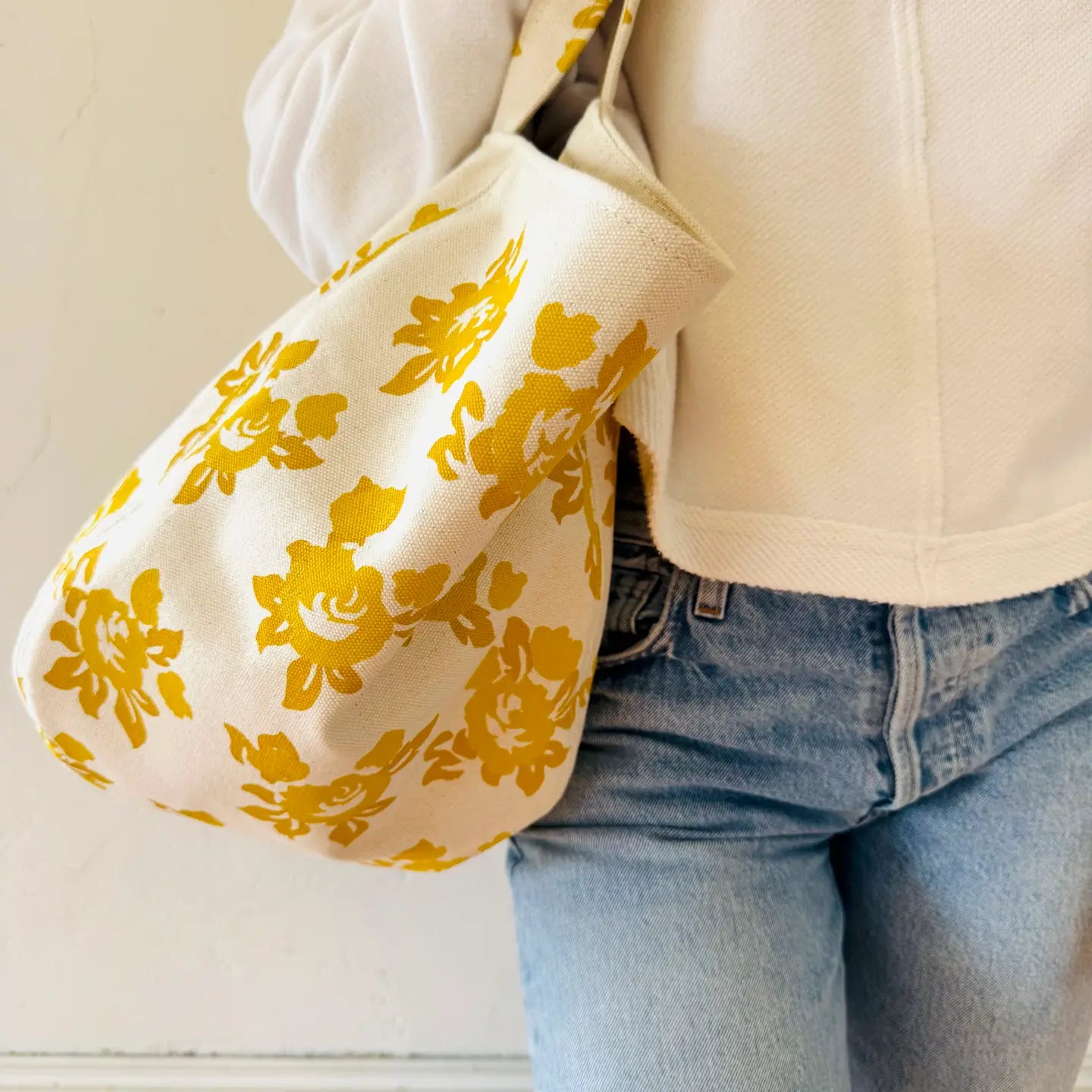 Person wearing a beige jacket with a yellow floral pattern over the shoulder against a neutral background