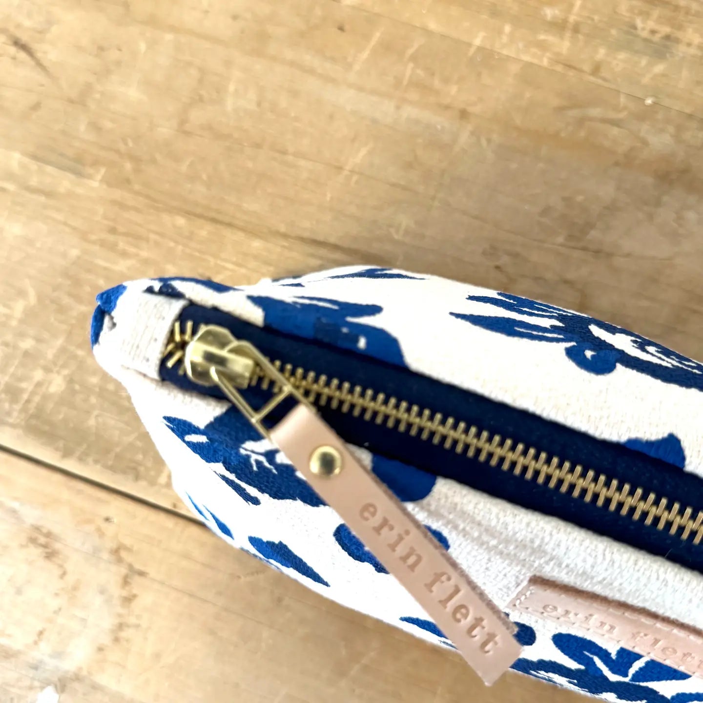 Pouch with blue floral pattern and gold zipper on a wooden surface