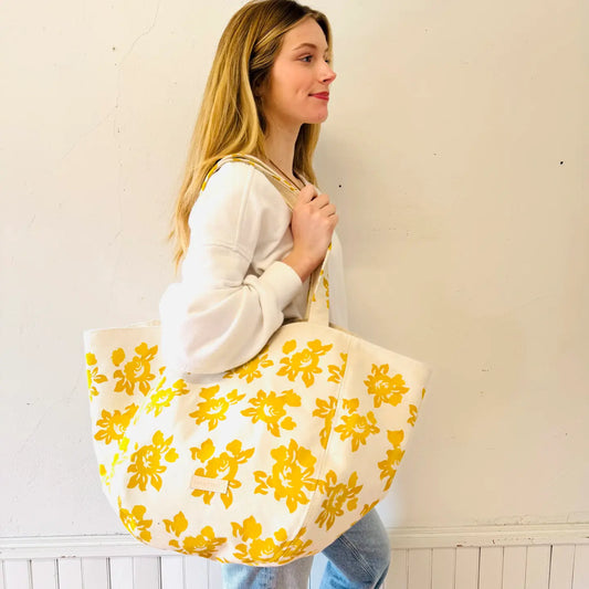 Woman holding a large tote bag with yellow floral pattern against a white wall.