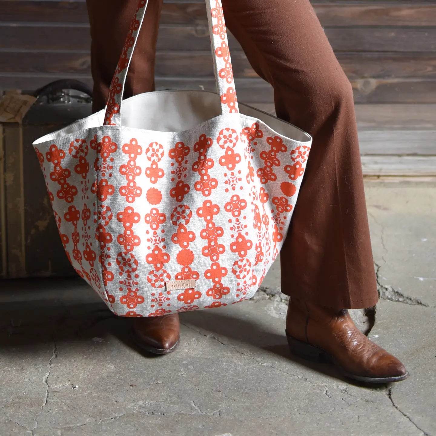Person holding a large tote bag with a red floral pattern on a stone surface.