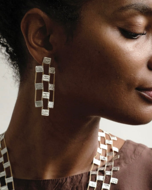 Headshot of dark skinned woman wearing checkerboard style sterling silver and brass earrings and necklace.