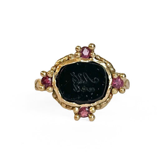 A black, carved intaglio with the message 'All's well' sits at the center of a yellow old ring surrounded with four rubies.