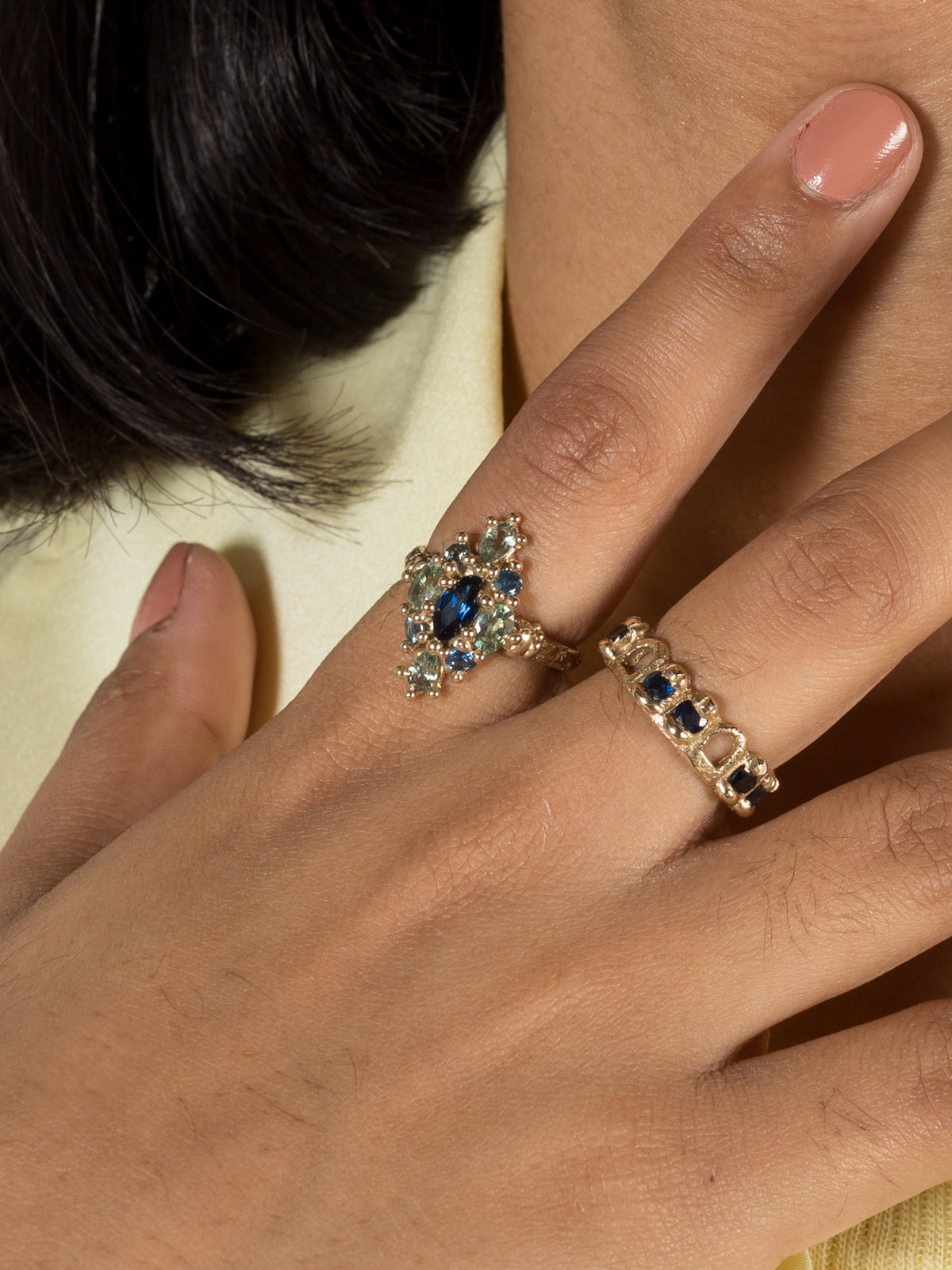 A model hand shown wearing a yellow gold ring with blue and green sapphires.
