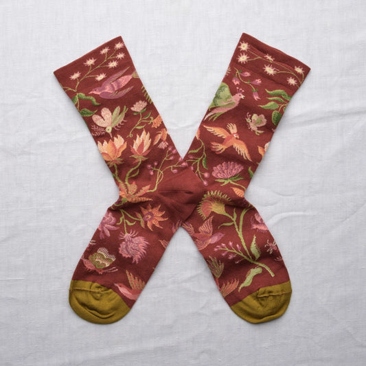Pair of maroon socks with floral and bird pattern on a light gray background