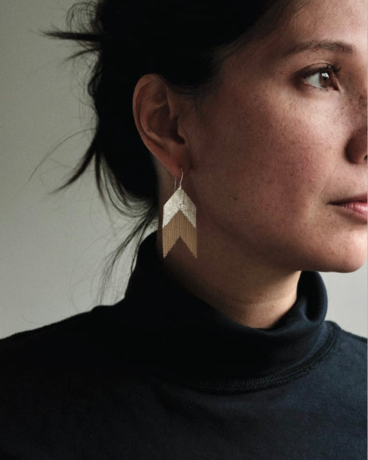 Headshot of light skinned woman with brown hair tied back wearing a chevron shaped silver and brass earring.
