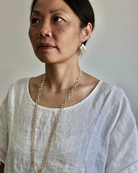 Cropped image of woman with long dark hair wearing a white round neck shirt and, silver earrings and a long silver and brass chain necklace.