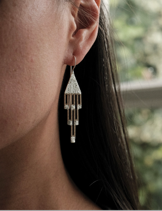 Cropped side headshot of woman with long dark hair waering a sterling silver and brass chain earring.